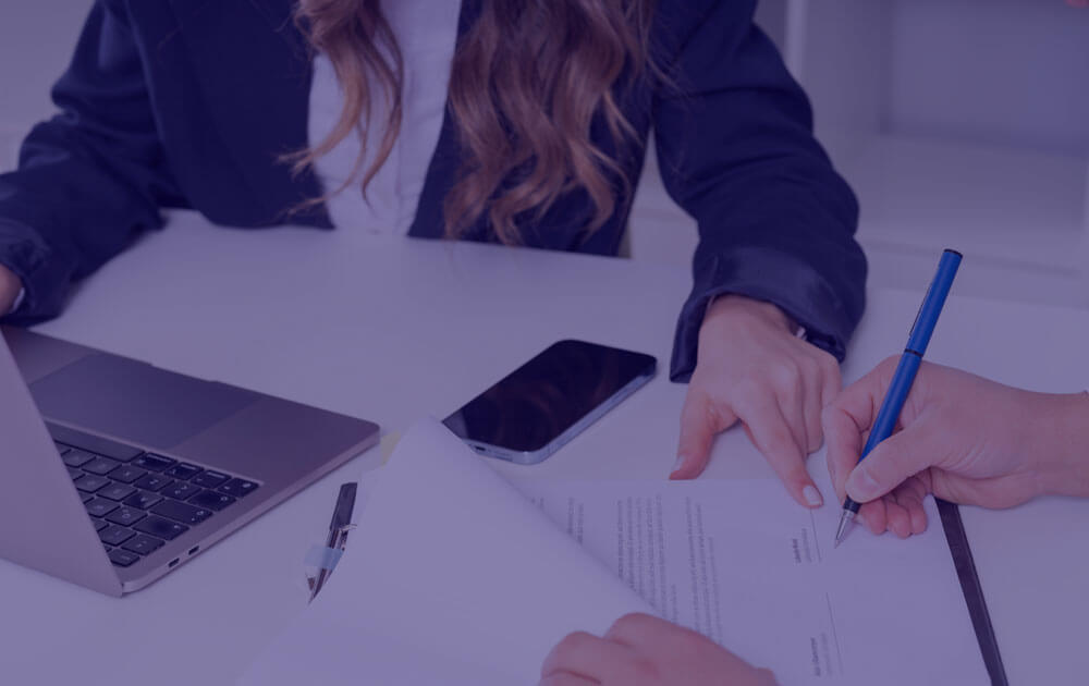 A woman pointing to a form a man is signing